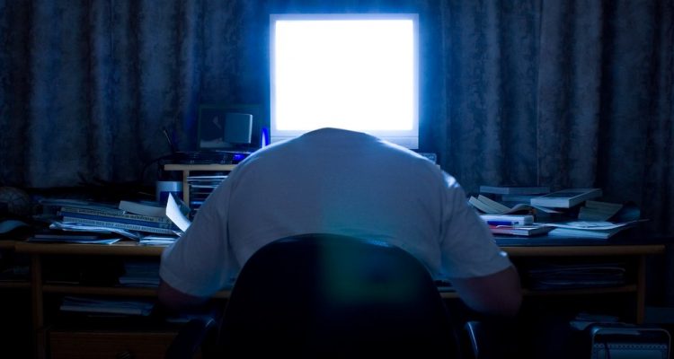 A headless man at a cluttered desk with glowing computer screen