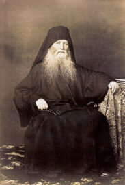 Portrait of Elder and Spiritual Father Ieronim, seated next to a table with books, and holding a prayer rope.